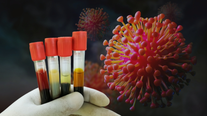 A hand holds blood samples with an illustration of the coronavirus in the background