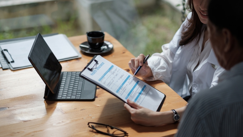 Two people sit at a table reviewing a health insurance form, with a tablet and documents nearby