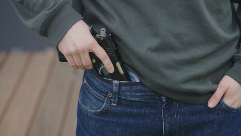 Person puts a handgun in their waistband, showing a concern from Firearms Now the Leading Cause of Death for US Children