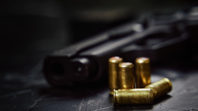 A handgun and bullets lie on a dark surface