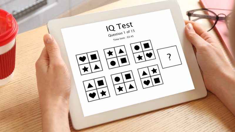 A person holds a tablet displaying a visual pattern recognition question for an IQ test