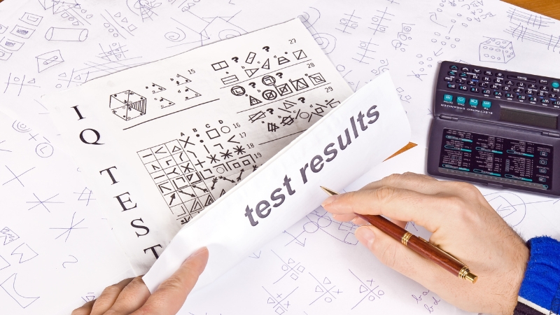 A person's hands are reviewing an "IQ Test" sheet with "test results" visible, alongside other papers and an electronic organizer