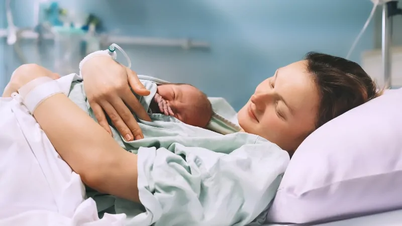 A young mother rests in a hospital bed holding her newborn, representing real stories behind the 2025 teen birth rates