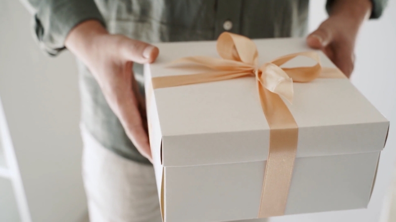 A person holds a neatly wrapped gift box with a ribbon, reflecting gift spending habits across U.S. demographics