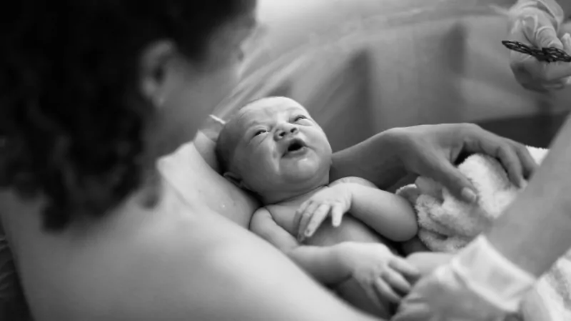 A newborn is held in a birthing tub by a young mother and a support person during a water birth