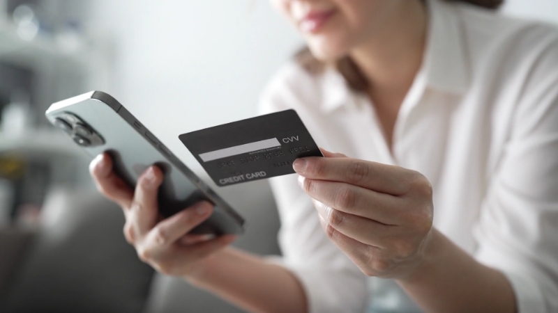 A woman holds a credit card and smartphone while making an online payment or checking loan details