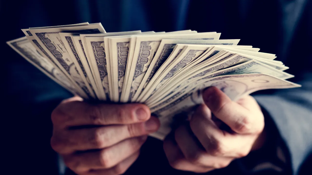 A person holds a fan of U.S. dollar bills in both hands