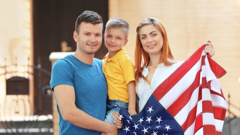 A smiling family holds an American flag together, highlighting questions about supporting families in the U.S. future