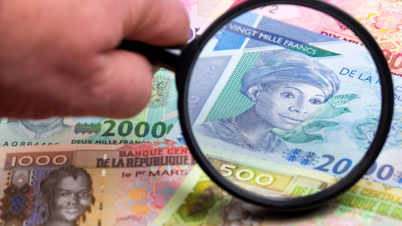 A hand holding a magnifying glass over Guinean Franc banknotes