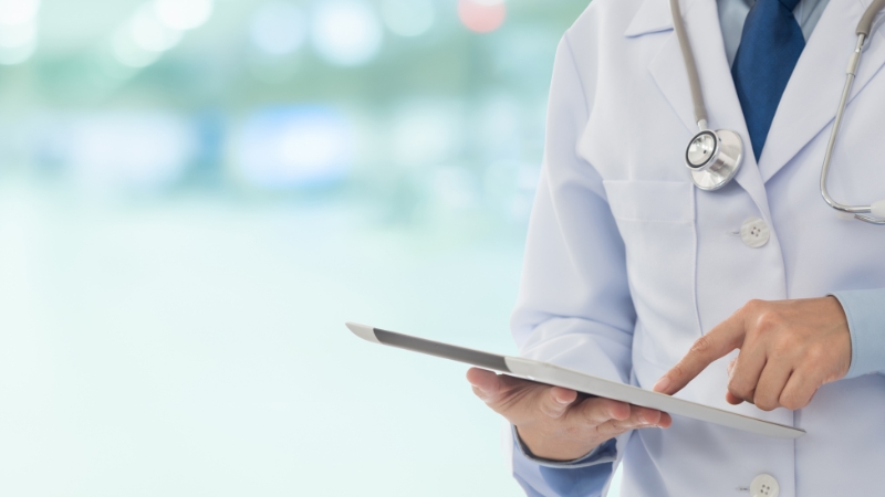 A doctor in a white coat uses a tablet to review patient records in a secure healthcare setting