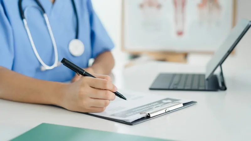 A healthcare worker fills out a form on a clipboard next to a tablet, collecting data for large health surveys