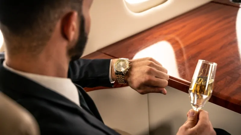 A man in a private jet looks at his gold watch and holds champagne, showing a lifestyle common among billionaires in 2025 America
