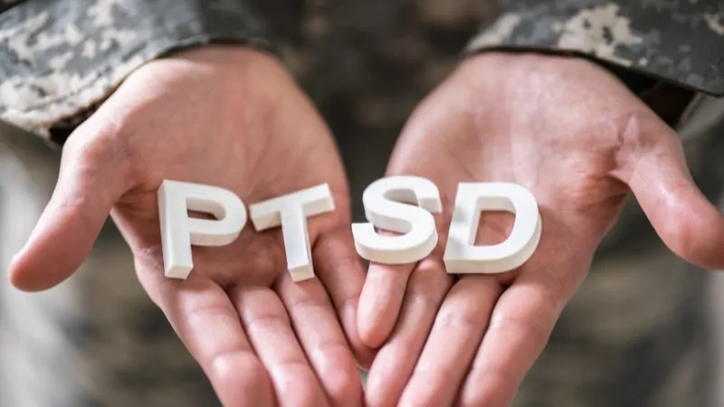 A person in military uniform holds letters spelling PTSD