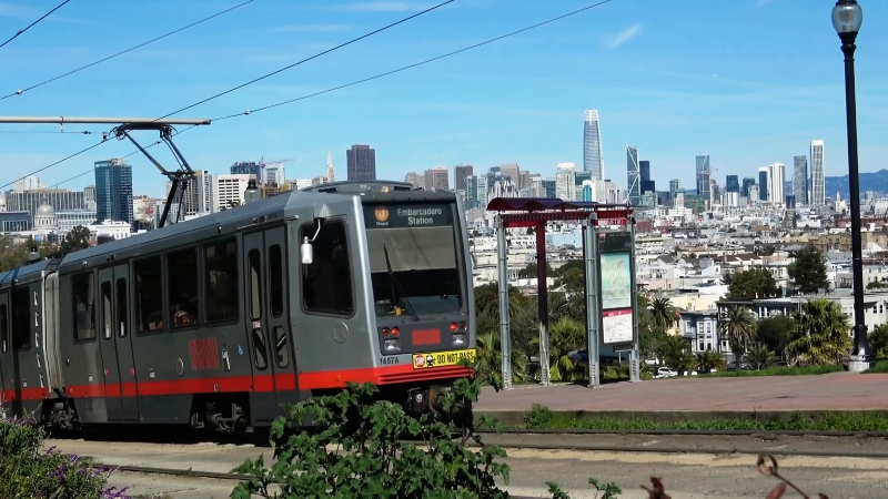 A Muni train in San Francisco with the city skyline in the background