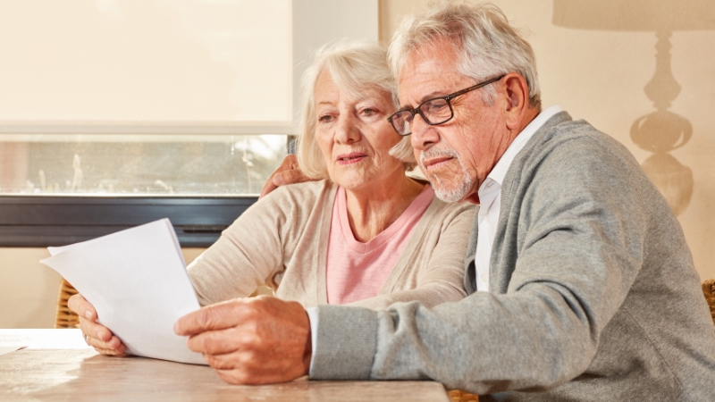 An elderly couple sits together reviewing paperwork about the average age of retirement in the United States