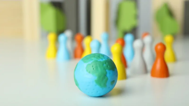 Colorful game pieces stand behind a small globe on a white table, symbolizing world population growth trends