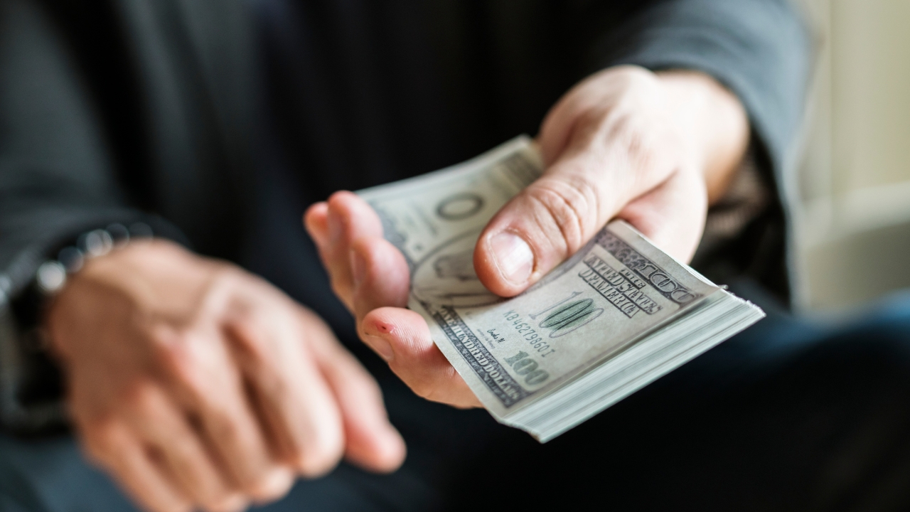 A person hands over a stack of U.S. dollar bills