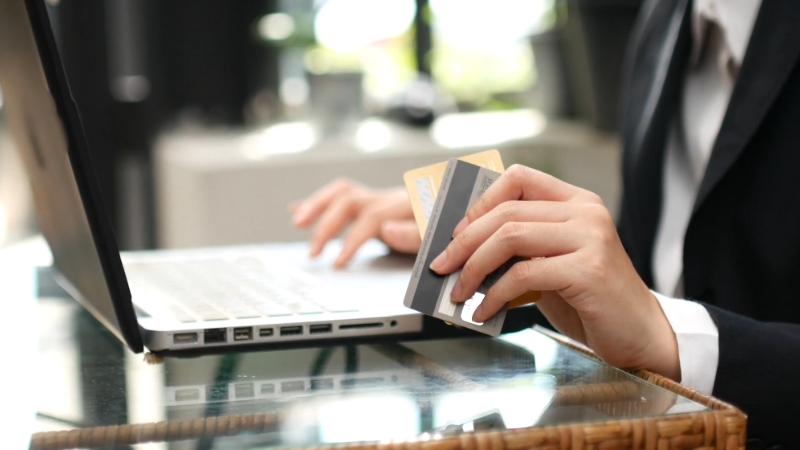 A person holding credit cards while using a laptop to explore borrowing options online