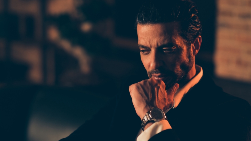 A man sits in deep thought wearing a suit and watch, reflecting on wealth and what it means to be a billionaire