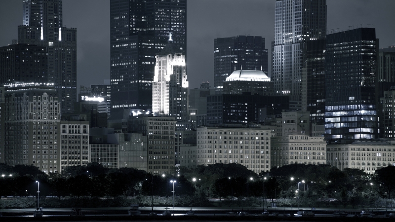 A nighttime view of a Midwestern city skyline with tall buildings lit up against a dark sky