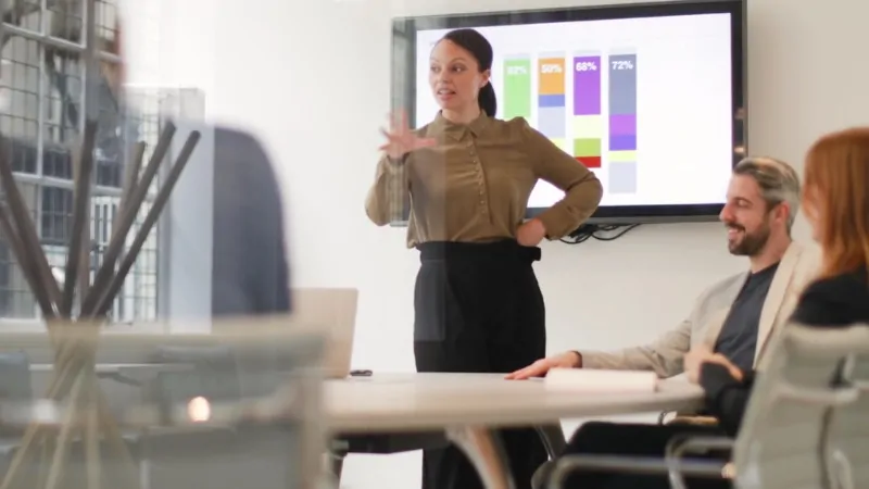 A businesswoman presents data to colleagues in a meeting room, illustrating growth trends for the best startups