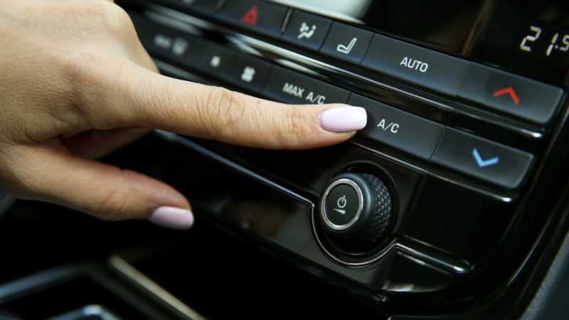A person’s hand presses the A/C button on a car dashboard