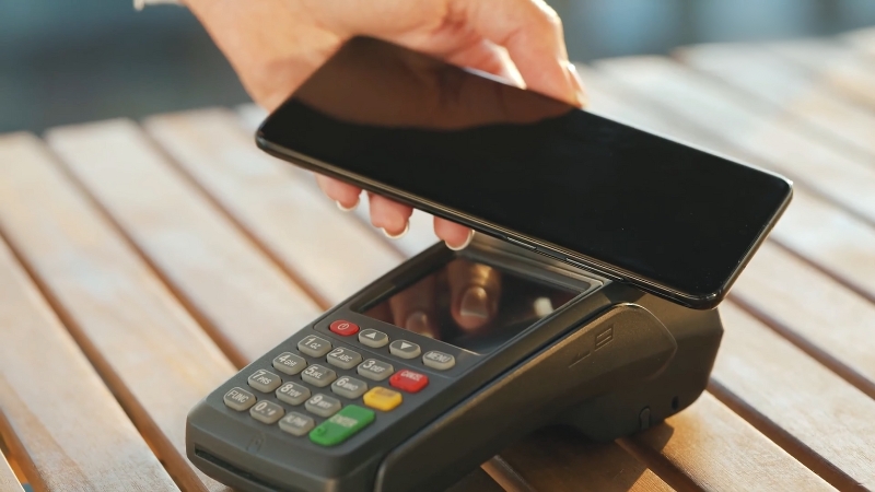 A person makes a contactless payment with a smartphone at a card reader terminal