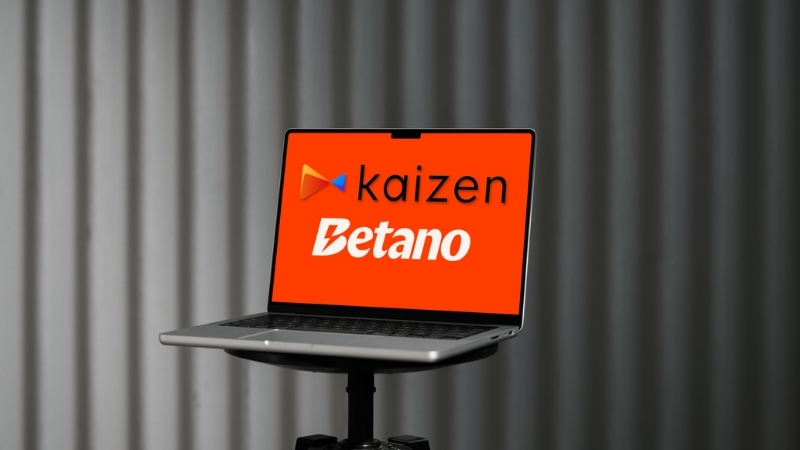 A laptop screen displays the Kaizen and Betano logos on a bright red background