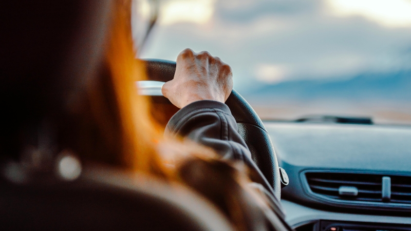 A person drives a car with one hand on the steering wheel as cool air flows through the front vents