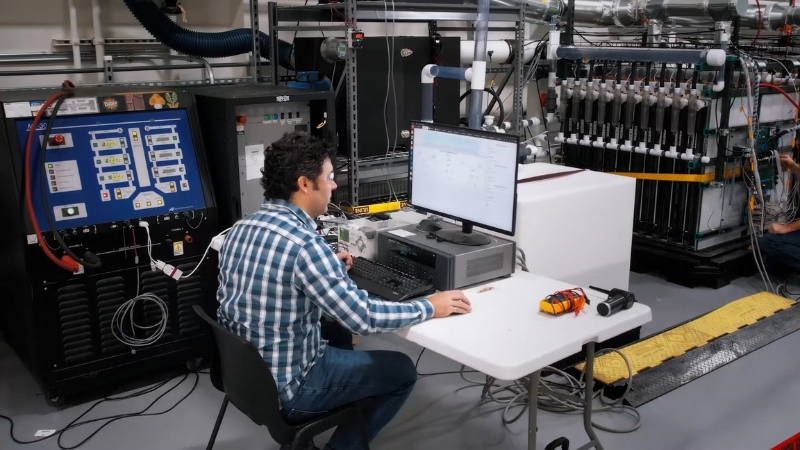 An engineer works at a computer station inside Form Energy’s lab with battery testing equipment in the background