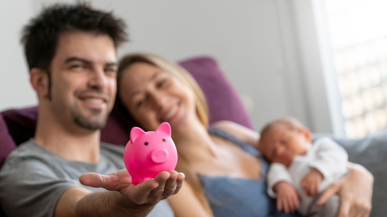 A couple sits with their baby and a pink piggy bank