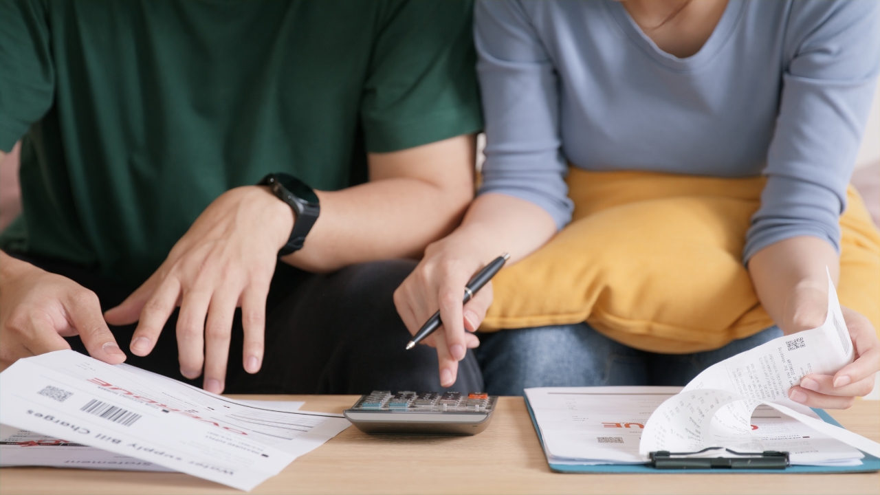 Two people review bills and receipts with a calculator on a table