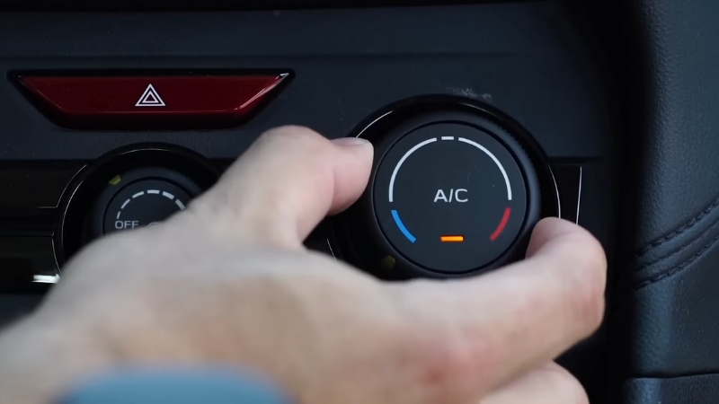A person adjusts the car’s A/C temperature dial, showing the blue and red cooling and heating zones