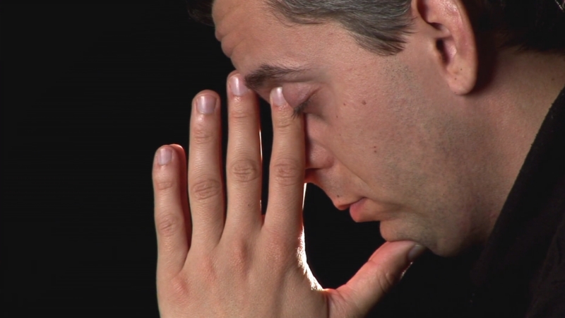 A man sits with his hand on his face, showing the emotional weight and human reality behind stress in America