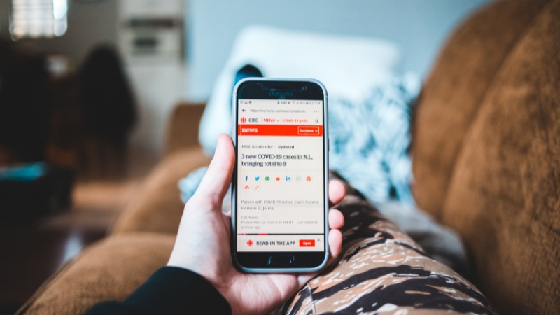 A person holding a smartphone displaying a health news article while sitting on a couch