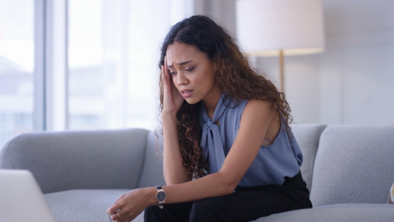 A stressed woman sitting on a couch holding her head, illustrating the growing problem of stress in America