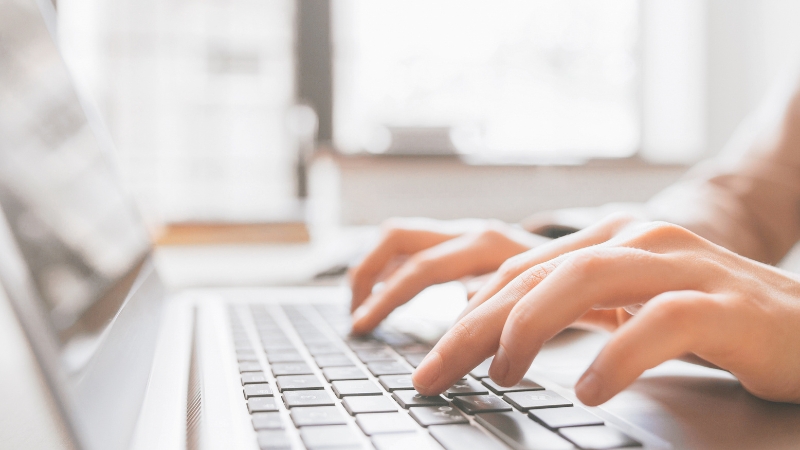 Close-up of a person typing on a laptop keyboard in natural light