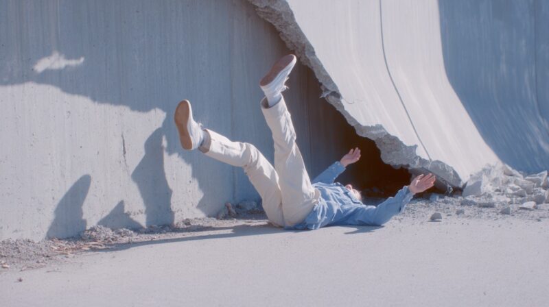 Person falling backward on the ground near a broken concrete structure, representing fall-related injuries