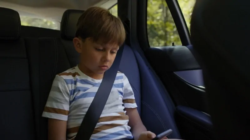 A young boy secured with a seat belt in the back seat of a car, illustrating car seat laws