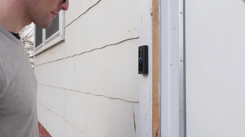 A person stands in front of a smart video doorbell installed on a house wall
