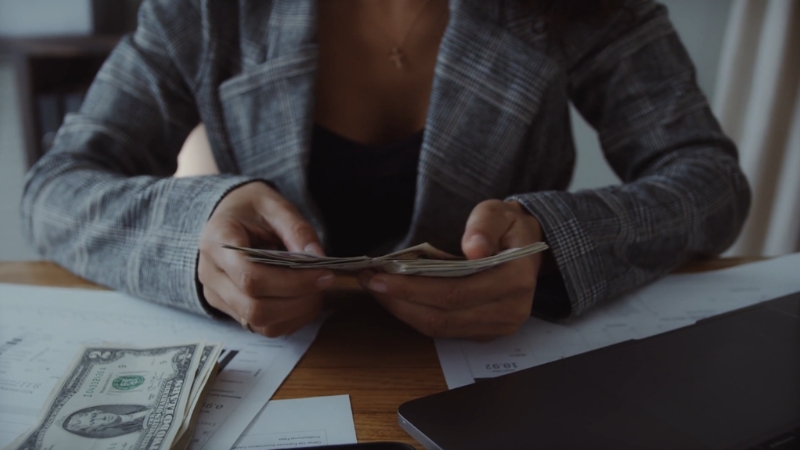 Person counting dollar bills at a desk with financial papers showing federal revenue and spending data