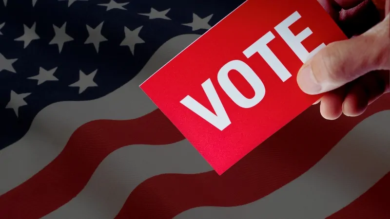 Hand holding a red vote card in front of the U.S. flag, showing being registered to vote