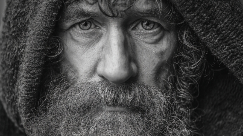 Close-up portrait of an older homeless man with a hood