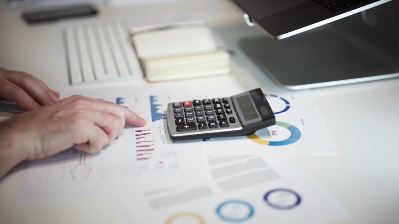 Person using a calculator on financial charts showing data about federal revenue