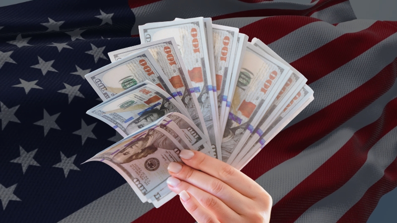 Hand holding U.S. dollars with an American flag background showing federal revenue across states