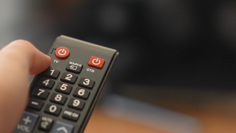 A person holds a TV remote while preparing to switch between streaming platforms