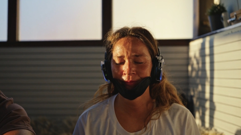 A woman with headphones and a face strap sits with closed eyes during a focused breathwork session