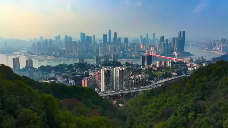 A daytime view of Chongqing with dense towers rising above the river and hills