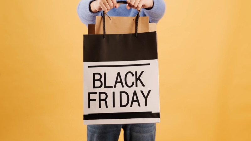 A shopper holds a large black friday bag against a bright background