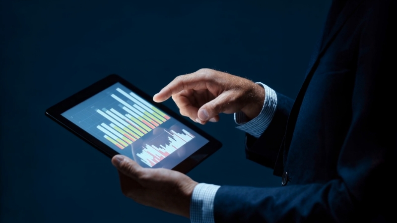 A person reviews colorful economic charts on a tablet screen